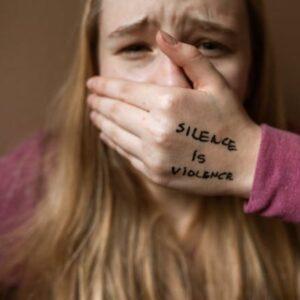 Mujer En Camisa Morada Que Cubre Su Rostro Con Su Mano Donde Pone "Silence is Violence"